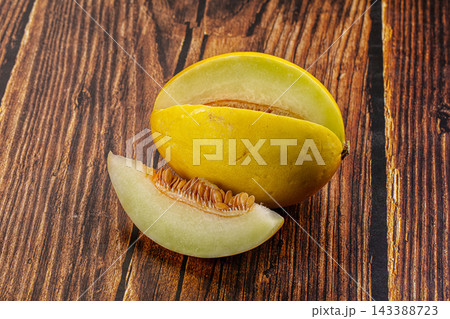 Whole honeydew melon with cut slice showing pale green flesh and seeds on rustic dark brown wooden table, fresh summer fruit close up Whole honeydew melon with cut slice showing pale green flesh and seeds on rustic dark brown wooden table, fresh summer fruit close up 143388723