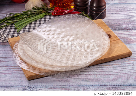 Uncooked rice paper round sheets on wooden cutting board with herbs and spices for Asian cuisine preparation Uncooked rice paper round sheets on wooden cutting board with herbs and spices for Asian cuisine preparation 143388884