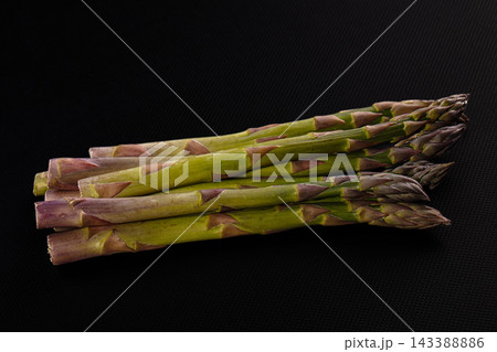 Dark matte surface, green and purple asparagus spears, fresh vegetable bundle Dark matte surface, green and purple asparagus spears, fresh vegetable bundle 143388886