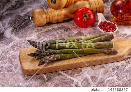 Marble countertop with green asparagus spears on wooden cutting board, fresh vegetable culinary composition 143388887