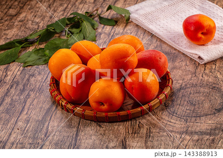 Fresh apricots in woven basket on rustic wooden table with green leaves and cloth napkin 143388913