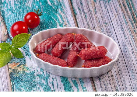 Mini piccolini salami sausages in white ceramic bowl with cherry tomatoes and basil leaves on rustic turquoise wooden table, cured meat snack 143389026