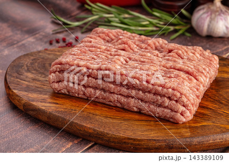 Raw minced pork block on round wooden cutting board with fresh rosemary sprigs and garlic bulb background ingredient preparation Raw minced pork block on round wooden cutting board with fresh rosemary sprigs and garlic bulb background ingredient preparation 143389109
