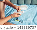 Close-up of a woman hand preparing a sterile gauze bandage for dressing an injured leg at home. Medical supplies and scissors are visible, illustrating first aid, wound care, home treatment 143389737