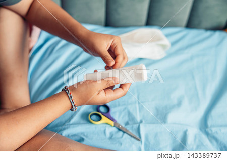Close-up of a woman hand preparing a sterile gauze bandage for dressing an injured leg at home. Medical supplies and scissors are visible, illustrating first aid, wound care, home treatment 143389737