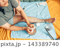 plus size young woman performing home wound care for a bruised and injured leg while sitting on a bed with gauze pads, bandages, and a crutch nearby, illustrating recovery, first aid, and 143389740