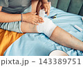 person applying a bandage to an injured knee during first aid at home with close up view of wound care and recovery process. concept of healthcare, rehabilitation, family medicine, pediatric care 143389751