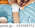person cutting medical bandage from leg after surgery, home wound care on bed with blue sheet, yellow blanket, recovery process, healthcare, medical service, rehabilitation, top view 143389752