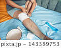 person cutting medical bandage from leg after surgery, home wound care on bed with blue sheet, yellow blanket, recovery process, healthcare, medical service, rehabilitation 143389753