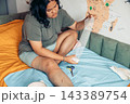 plus size young woman sitting on a bed and applying a gauze bandage to her injured leg at home. visible scars and bruising on the knee and thigh. home first aid, wound care, injury recovery 143389754