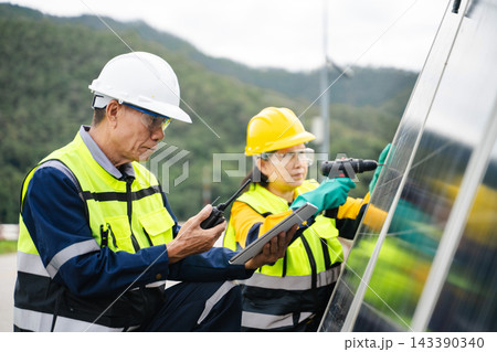 Asian engineers in hardhats and safety vests inspect and install photovoltaic solar panels along a mountain roadside for clean energy. Asian engineers in hardhats and safety vests inspect and install photovoltaic solar panels along a mountain roadside for clean energy. 143390340