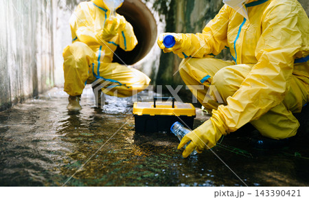 Environmental inspectors in yellow protective gear collect water runoff in glass bottles and flasks 143390421
