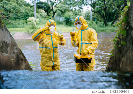 Environmental scientists in yellow protective suits analyze polluted water samples in glass flasks Environmental scientists in yellow protective suits analyze polluted water samples in glass flasks 143390462