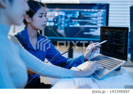 Two female programmers collaborate late in a modern tech office, analyzing computer code on screens to optimize software development Two female programmers collaborate late in a modern tech office, analyzing computer code on screens to optimize software development 143390897
