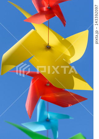 A close-up view showcasing a vertical arrangement of colorful plastic windmill-shaped pinwheels against a clear blue sky 143392097