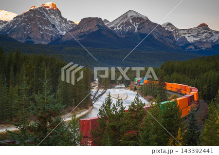 Majestic freight train carrying cargo travels through peaceful mountain forest and river in canada offering serene wilderness journey 143392441