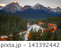 Serene freight train travels through mountain forest along river in Canada showcasing peaceful wilderness scenery during sunset 143392442