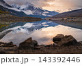 Serene mountain landscape in canada shows peaceful nature with snowy peak reflection on calm lake water beyond rocky shore at sunset 143392446