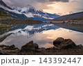 Serene lake reflection captures peaceful mountain wilderness landscape scenery at sunset in Canada under dramatic snow peak sky 143392447