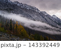 Dramatic mountain peak rises above thick fog and autumn forest covering rough rock during peaceful morning in majestic canada 143392449