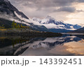 Tranquil mountain landscape with snow reflection in calm lake water and scenic cloud over peaceful wild nature of majestic canada 143392451
