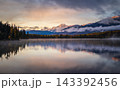 Serene sunrise illuminates snow mountain forest and calm lake reflection creating peaceful tranquil scenic wilderness in canada 143392456