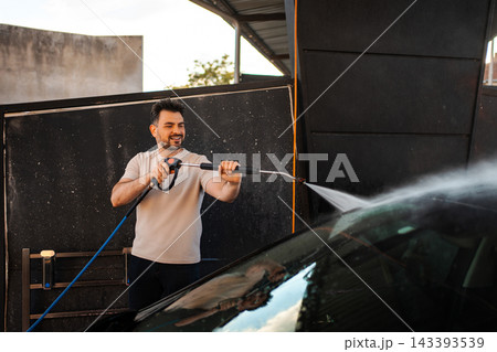 Happy man washing car with pressure washer outdoors Happy man washing car with pressure washer outdoors 143393539