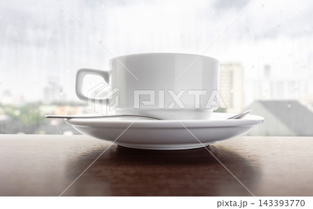 White coffee cup on saucer with spoon on wooden table by window White coffee cup on saucer with spoon on wooden table by window 143393770