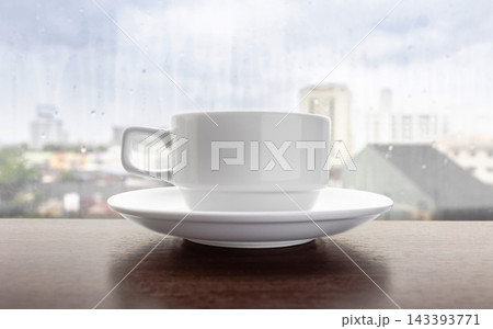 White coffee cup on wooden table by rainy window 143393771