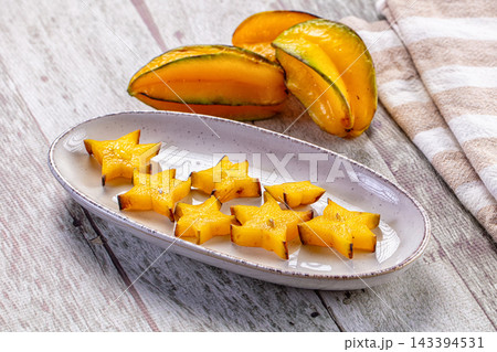 Sliced yellow star fruit pieces arranged on speckled ceramic plate with whole carambola on rustic wood table tropical fruit Sliced yellow star fruit pieces arranged on speckled ceramic plate with whole carambola on rustic wood table tropical fruit 143394531