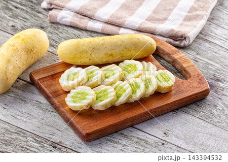 Sliced yellow cucumber on wooden cutting board with whole cucumbers and striped cloth background food preparation Sliced yellow cucumber on wooden cutting board with whole cucumbers and striped cloth background food preparation 143394532