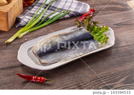White ceramic plate with two salted herring fillets on lettuce, green onions and red chili peppers nearby, seafood preparation 143394533