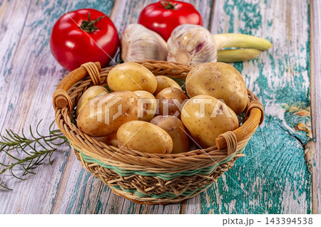 Fresh potatoes in a wicker basket with tomatoes, garlic, and herbs on a rustic wooden table Fresh potatoes in a wicker basket with tomatoes, garlic, and herbs on a rustic wooden table 143394538