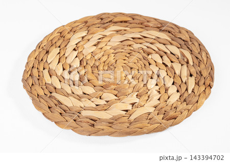 Round woven water hyacinth placemat in natural beige and cream tones on white background, rustic tableware for eco friendly dining 143394702