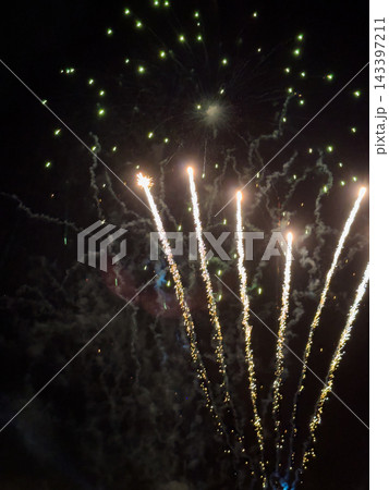 Bright golden trails and green sparks illuminate the dark night sky during a festive fireworks show with sparkling pyrotechnic displays filling the air with light and celebratory smoke effect Bright golden trails and green sparks illuminate the dark night sky during a festive fireworks show with sparkling pyrotechnic displays filling the air with light and celebratory smoke effect 143397211