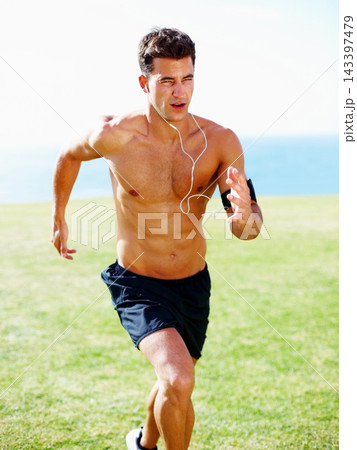 Man, running and earphones or outdoor workout for streaming music, subscription or podcast. Male person, sprint and grass field for cardio health or marathon training with playlist, practice or speed 143397479