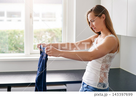 Housework, cleaning and woman folding laundry, organising clothes and apparel washing in kitchen. Lady, jeans and housekeeping hygiene with clothing during morning chores routine in the lounge 143397699