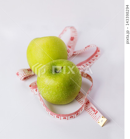 Two fresh green apples with a measuring tape on a clean white surface, representing healthy eating, weight management, nutrition, fitness, and wellness lifestyle concepts Two fresh green apples with a measuring tape on a clean white surface, representing healthy eating, weight management, nutrition, fitness, and wellness lifestyle concepts 143398294