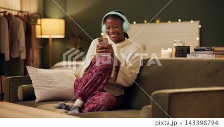 African woman, headphones and phone on sofa with smile, laugh and excited for music in home living room. Girl, smartphone and happy for streaming, audio subscription and mobile app on couch in house 143398794