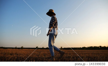 Adult agronomist in straw hat walking among barley plantation at dusk. Female farmer going through wheat meadow at sunset. Beautiful scenic landscape. Concept of agricultural business. Slow motion Adult agronomist in straw hat walking among barley plantation at dusk. Female farmer going through wheat meadow at sunset. Beautiful scenic landscape. Concept of agricultural business. Slow motion 143399030
