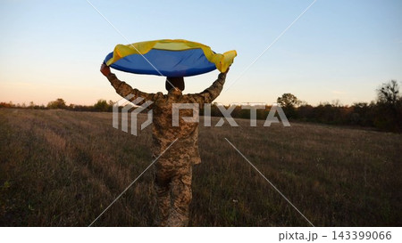 Soldier of ukrainian army running with raised flag Ukraine above his head at field. Young male military in uniform jogging with blue-yellow banner at meadow. Victory against russian aggression Soldier of ukrainian army running with raised flag Ukraine above his head at field. Young male military in uniform jogging with blue-yellow banner at meadow. Victory against russian aggression 143399066
