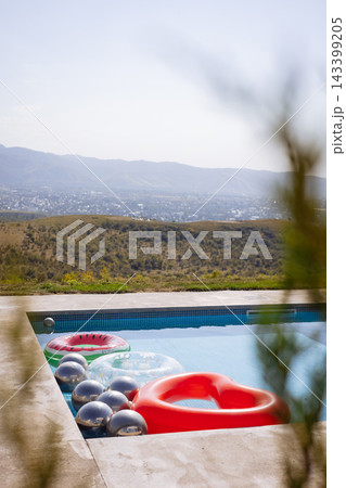 Bright inflatable toys in infinity pool with mountain and city valley view on clear summer day Bright inflatable toys in infinity pool with mountain and city valley view on clear summer day 143399205