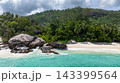 Granite boulders situated by turquoise ocean waters, set against lush forested hills. Seychelles, Mahe. Roche Copra. 143399564