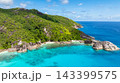 Expansive green hills covered in dense vegetation meet the wide expanse of clear blue ocean with rocky formations. Seychelles, Mahe. 143399575