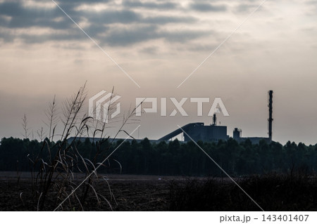 Factories and tall smokestacks stand alone amidst agricultural and wasteland areas Factories and tall smokestacks stand alone amidst agricultural and wasteland areas 143401407