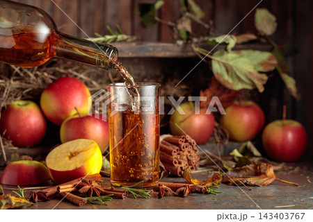 Apple juice on an old kitchen table next to fresh apples, cinnamon, anise, and rosemary. Apple juice on an old kitchen table next to fresh apples, cinnamon, anise, and rosemary. 143403767
