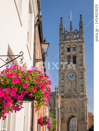 The tower of St Mary's Church, a large historic church located in central Warwick, UK. Focus on a hanging basket of flowers in the foreground. 143403929