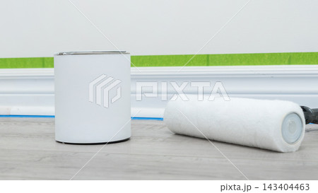Home renovation mockup featuring a paint can and roller on wooden flooring with painter's tape and wall preparation visible Home renovation mockup featuring a paint can and roller on wooden flooring with painter's tape and wall preparation visible 143404463