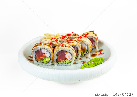 Sushi roll with tuna, salmon, shrimp and cucumber topped with baked spicy sauce, red tobiko and unagi sauce on white plate, white background Sushi roll with tuna, salmon, shrimp and cucumber topped with baked spicy sauce, red tobiko and unagi sauce on white plate, white background 143404527