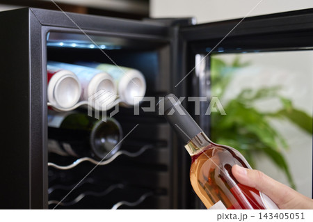 Woman placing bottle of rose wine into open wine cooler with other bottles inside Woman placing bottle of rose wine into open wine cooler with other bottles inside 143405051
